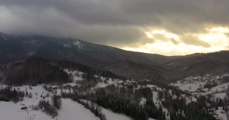 Vista-Aérea-De-Montañas-Y-Bosques-Cubiertos-De-Nieve-Al-Atardecer-En-Invierno