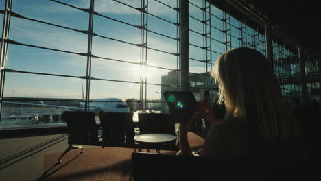 Der-Passagier-Benutzt-Das-Tablet-Im-Terminal-Des-Flughafens-Das-Fenster-Zeigt-Einen-Fliegenden-Verkehrsflugzeugbusi
