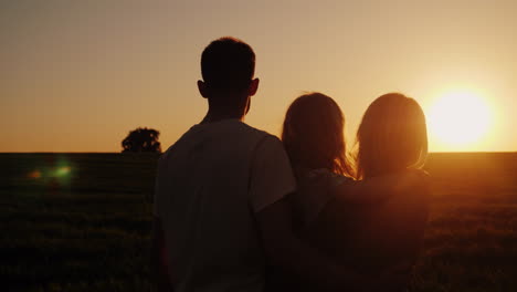 Eine-Dreiköpfige-Familie-Freut-Sich-Auf-Einen-Wunderschönen-Sonnenuntergang-4k-Video-Von-Hinten