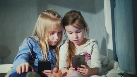 Zwei-Mädchen-Spielen-Auf-Smartphones-Sitzen-Nebeneinander-Auf-Dem-Bett-In-Deinem-Schlafzimmer-4k-Video