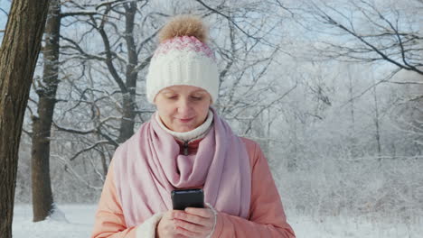 Junge-Frau-Geht-Im-Winterpark-Spazieren-Und-Genießt-Smartphone-4k-Zeitlupenvideo