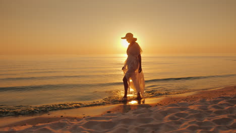 Eine-Frau-Mit-Hut-Und-Sommerkleid-Spaziert-Bei-Sonnenuntergang-Am-Meer