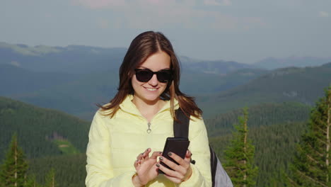Junge-Frau-Genießt-Ein-Smartphone-Vor-Einer-Malerischen-Kulisse-Von-Bergen,-Die-Immer-Mit-Wald-Bedeckt-Sind-Covered