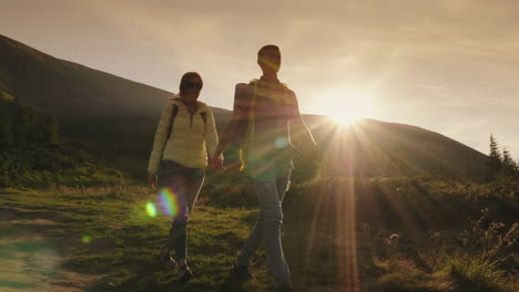 Young-Couple-Of-Tourists-Holding-Hands-Walking-Along-A-Montaña-Path-In-The-Rays-Of-The-Setting-Sun