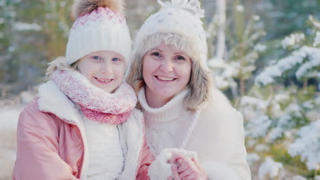 Winterporträts-Von-Mutter-Und-Tochter,-Die-Vor-Dem-Hintergrund-Der-Schneedecke-In-Die-Kamera-Lächeln