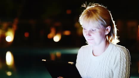 Attractive-Woman-Enjoys-The-Tablet-Late-In-The-Evening-Near-The-Pool