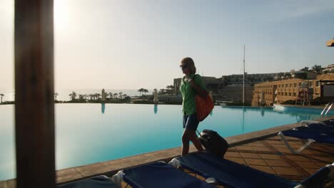 Steadicam-Shot-Of-Woman-With-Travel-Bag-Walking-On-Recreation-Area-Along-The-Pool