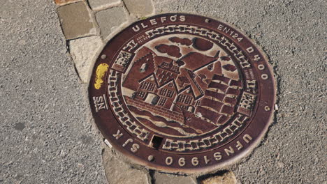 Metal-Sewer-Hatch-With-Images-Of-Houses-And-Sailboats-Original-Decoration-Of-The-City-In-Bergen