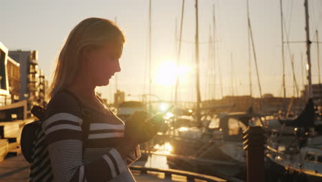 Silhouette-Einer-Frau-Mit-Einem-Smartphone-In-Der-Nähe-Des-Piers,-An-Dem-Viele-Yachten-Vor-Anker-Liegen