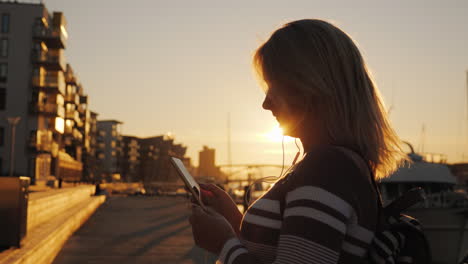Eine-Frau-Mit-Kopfhörern-Benutzt-Ein-Smartphone-Auf-Dem-Pier-Vor-Dem-Hintergrund-Privater-Yachten-Bei-Sonnenuntergang