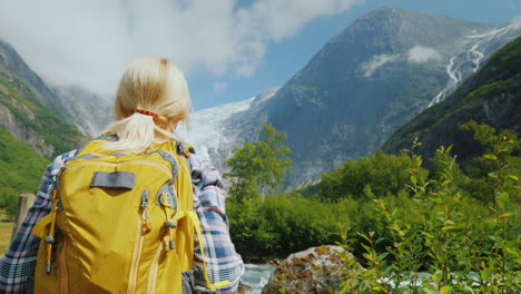 A-Tourist-With-A-Yellow-Backpack-Looks-At-A-Beautiful-Glacier-At-The-Top-Of-The-Mountain-Briksdal-Gl