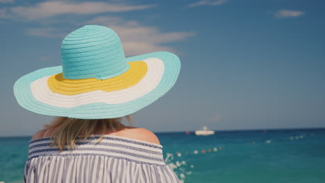 Eine-Frau-Mit-Hut-Betrachtet-Das-Azurblaue-Meer-Traum-Ferienkonzept-Rückansicht