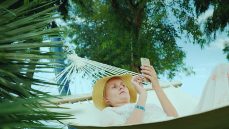 Mujer-Joven-Descansando-En-Una-Hamaca-Utilizando-Una-Conexión-De-Teléfono-Móvil-En-Concepto-De-Vacaciones-4k-Video