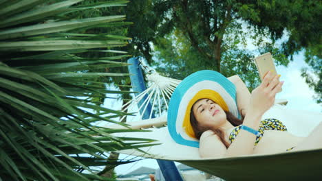 Enjoy-The-Rest-And-Be-Always-In-Touch-With-Friends-A-Girl-In-A-Cool-Hat-And-A-Bathing-Suit-Sunbathin