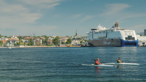 Ein-Paar-Ruderer-Schwimmen-In-Einem-Kajak-Vor-Dem-Hintergrund-Der-Stadtlinie-Von-Oslo