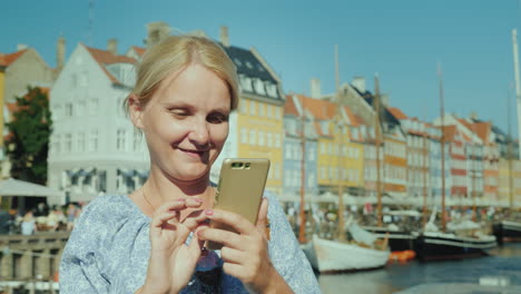 Eine-Glückliche-Frau-Benutzt-Ein-Smartphone-Steht-Vor-Dem-Hintergrund-Des-Kanals-Und-Der-Beliebten-Touristenstraße