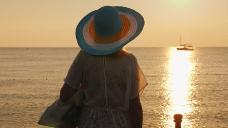 A-Young-Woman-In-Beach-Clothes-And-A-Wide-Brimmed-Hat-Is-Enjoying-The-Sunrise-On-The-Seashore-Going-