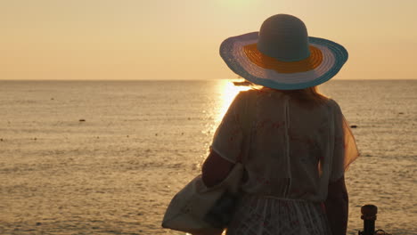 A-Slender-Tourist-Meets-The-Dawn-On-The-Sea-With-A-Bag-On-Her-Shoulder-And-A-Broad-Brimmed-Hat-On-He