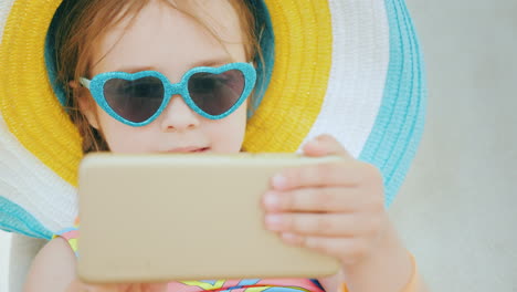 A-Cool-Girl-In-Sunglasses-In-The-Shape-Of-A-Heart-Uses-A-Smartphone-On-Vacation-4k-Video