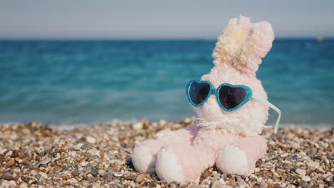 Pink-Hare-In-Sunglasses-Sits-On-Pebbles-Against-A-Blue-Sea