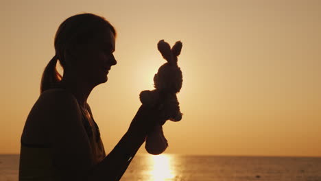 Silhouette-Eine-Frau-Spielt-Mit-Einem-Spielzeughasen-Im-Morgengrauen-Erinnere-Mich-An-Kindheit-4k-Video