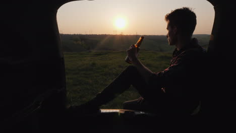 A-Teenager-Sits-In-The-Trunk-Of-A-Car-And-Drinks-Beer-From-A-Bottle