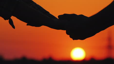 Man-And-Woman-Holding-Hands-Against-The-Sunset-And-Red-Sky