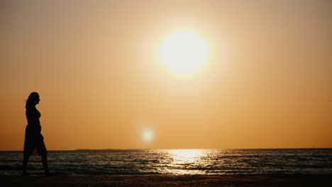 Die-Silhouette-Einer-Frau,-Die-Bei-Sonnenuntergang-Am-Meeresufer-Entlang-Geht