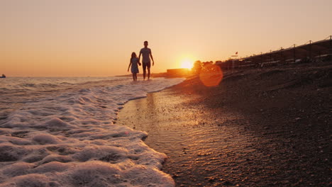 Brother-And-Younger-Sister-Walking-Along-The-Seashore-At-Sunset