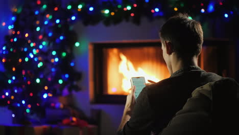 Junger-Mann-Benutzt-Ein-Smartphone-Am-Weihnachtlich-Geschmückten-Kamin