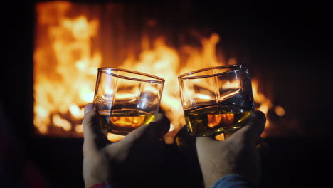 Zwei-Männliche-Hände-Mit-Gläsern-Whisky-Mit-Eis-Auf-Dem-Hintergrund-Der-Kaminwinterflucht-Con