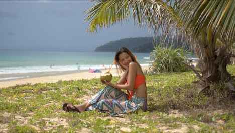Happy-woman-with-coconut-drink-resting-on-beach