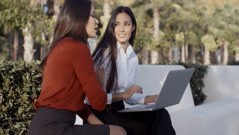 Dos-Mujeres-Bonitas-Compartiendo-Una-Computadora-Portátil-Al-Aire-Libre