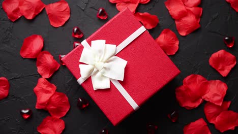 Geschenkbox-Auf-Schwarzem-Steintisch-Romantischen-Feiertagshintergrund-Mit-Rosenblättern