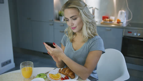 Smiling-woman-browsing-smartphone-during-breakfast