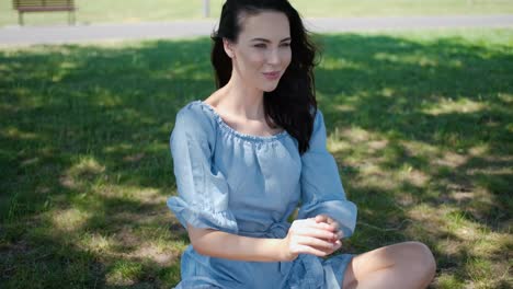 Portrait-of-attractive-brunette-woman-in-blue-dress-sitting-in-a-park