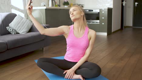 Young-attractive-sporty-woman-sitting-on-yoga-mat-making-selfie-with-her-mobile-phone