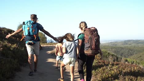 parents and kids wearing backpacks walking on path in mountains