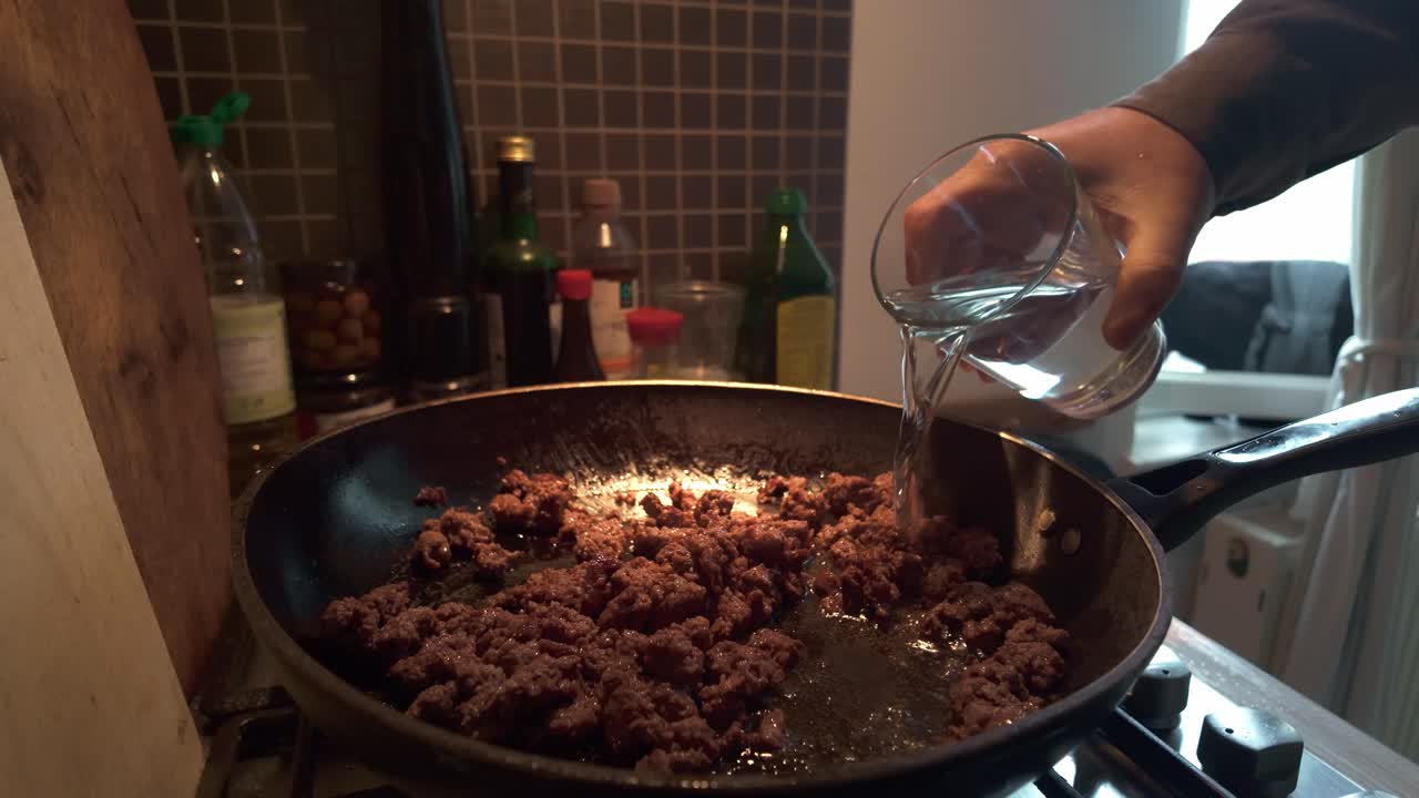 Home cook pouring water into frying pan of minced beef. Medium shot