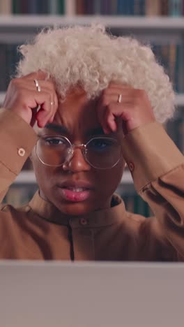 Young worried african american woman with laptop clutching head sits in library