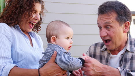 los abuelos sentados fuera de la casa jugando con el nieto bebé