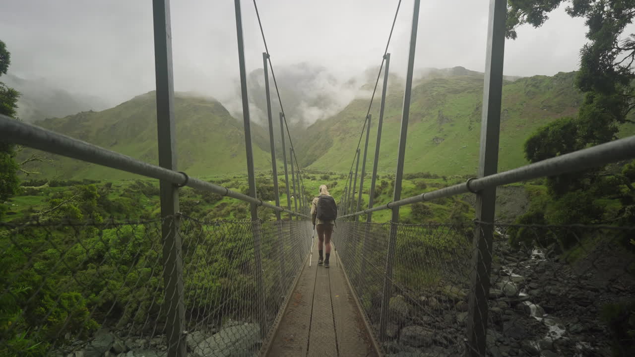 Woman hiking with nordic walking poles across suspension bridge on Rob Roy Glacier Trail
