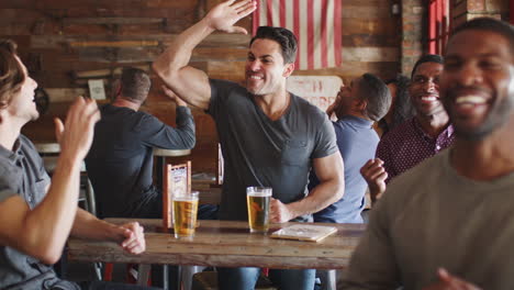 Group-Of-Male-Friends-Celebrating-Whilst-Watching-Game-On-Screen-In-Sports-Bar