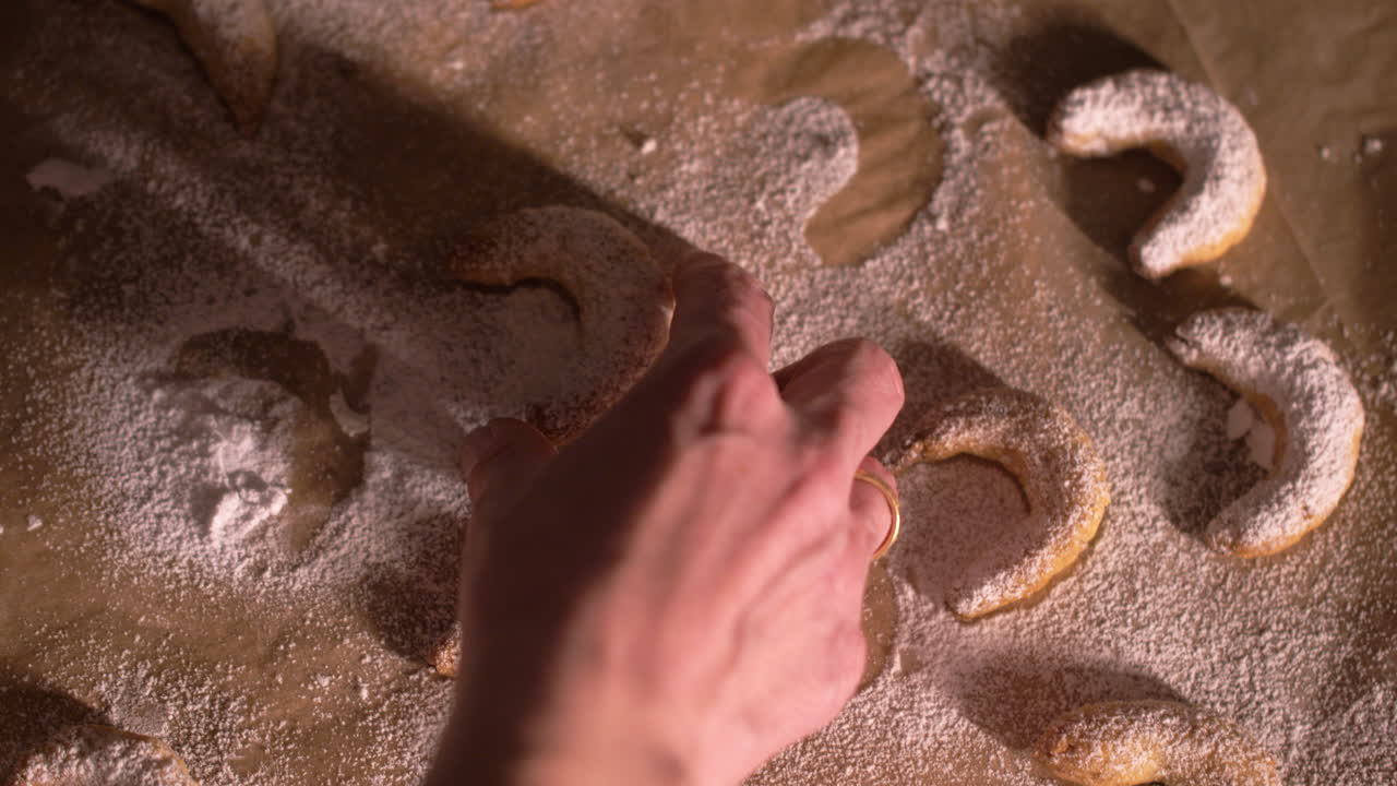 Top down, woman's hands pick up freshly baked crescent cookies from baking sheet