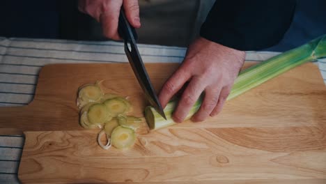 una persona cortando puerro fresco en una tabla de madera con limones y cebollas cerca