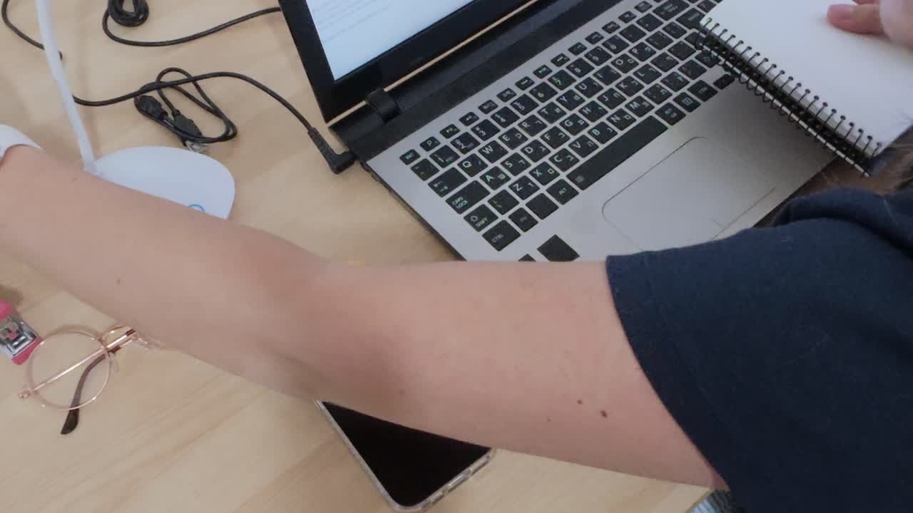 Close-up of hands multitasking, writing in notebook while using laptop