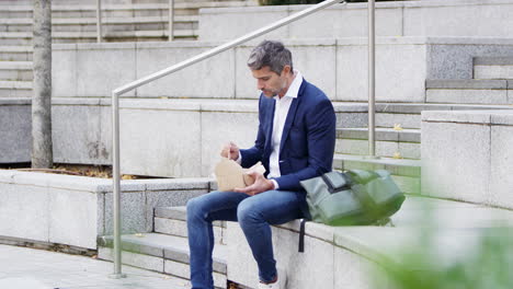 Hombre-De-Negocios-Sentado-Afuera-Durante-El-Almuerzo-Comiendo-Comida-Para-Llevar-De-Cartón-Reciclable-Sostenible