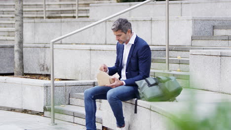 hombre de negocios sentado afuera en la pausa para el almuerzo comiendo comida para llevar de una caja de cartón reciclable sostenible