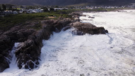 Frothing-seawater-and-crashing-waves-along-rocky-coastline-of-Hermanus,-aerial