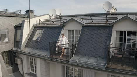 woman in white robe stands on rooftop balcony